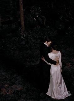 a bride and groom are standing in the woods at night, holding each other close together