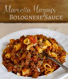 a white bowl filled with pasta and meat sauce on top of a wooden table next to a