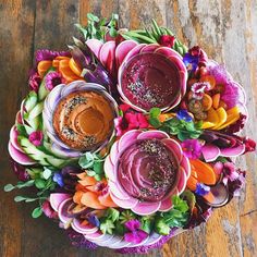 an arrangement of colorful flowers and dips on a wooden table with wood flooring