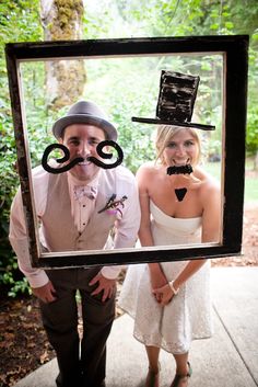 a man and woman standing next to each other in front of a picture frame with a mustache on it