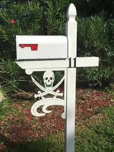 a white mailbox with a skull and cross on it in front of some bushes