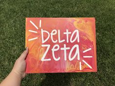 a hand holding up a sign that says delta zetta on it in the grass