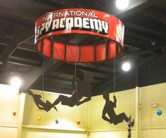 an indoor climbing gym with two people on the wall and one person hanging upside down