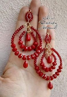 a person is holding some red beads in their hand and there are two pairs of earrings hanging from them