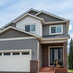 a house that is in the middle of some grass and dirt with two garage doors