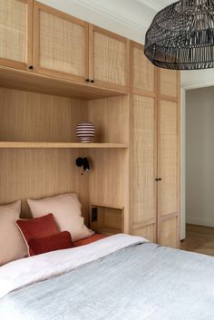 a bed sitting under a light next to a wooden shelf filled with pillows and blankets