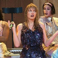 three women in sequins on stage with one holding a cell phone