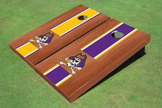 two purple and yellow striped cornhole game boards on green grass with white skull in center