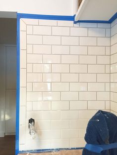 a bathroom being remodeled with blue tape on the wall and white subway tile behind it