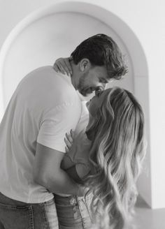 a man and woman kissing each other in front of a white wall with an arched doorway