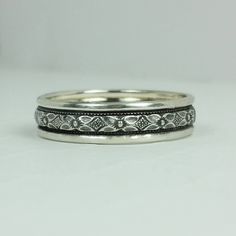 two wedding bands with intricate designs on each band, one in white gold and the other in silver