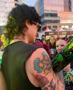 a woman with tattoos on her arm holding a beer bottle in front of other people