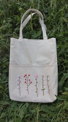 a white bag with embroidered flowers on it sitting in the middle of some green grass