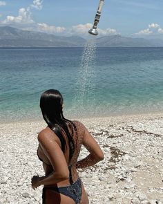 a woman in a bathing suit is spraying water on her head while standing on the beach