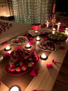 a wooden table topped with lots of plates and bowls filled with fruit next to candles