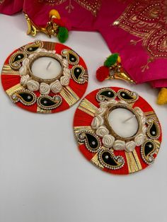 two red and gold decorated candles sitting on top of a white table next to a pink pillow