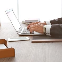 a man is typing on his laptop while sitting at a desk with other office supplies