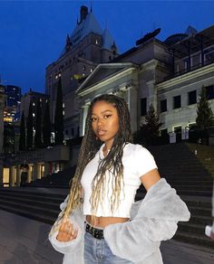 a woman with dreadlocks standing in front of some stairs and buildings at night