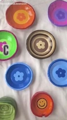 colorful bowls with smiley faces on them sitting on a white sheet in the middle of a circle