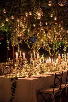 an outdoor dinner table with candles and greenery on the tables, surrounded by hanging lights