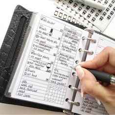 a person holding a pen in their hand next to an open planner with notes on it