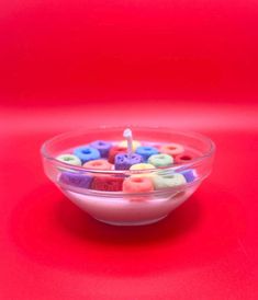 a bowl filled with lots of different colored buttons on top of a red table next to a lit candle