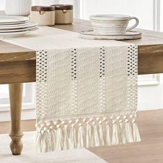 a white table runner with tassels and plates on it in front of a window