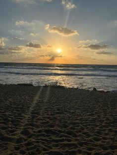 the sun is setting over the ocean with clouds in the sky and sand on the beach