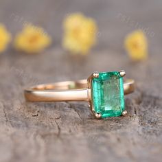 an emerald ring sitting on top of a piece of wood with yellow flowers in the background