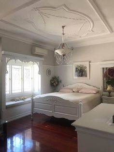 a white bed sitting in a bedroom on top of a hard wood floor next to a window