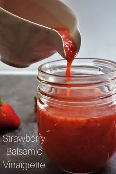 strawberry balsamic vinaigrete is being poured into a jar with strawberries