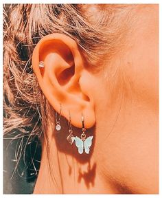 a close up of a person's ear with butterfly shaped earrings on top of it