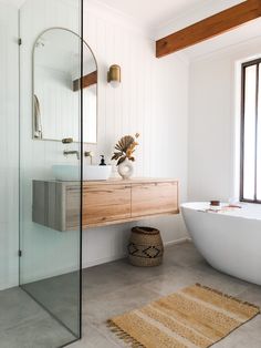 a white bath tub sitting next to a bathroom sink under a large glass shower door