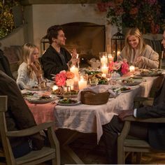 a group of people sitting around a dinner table with candles on the table and food in front of them