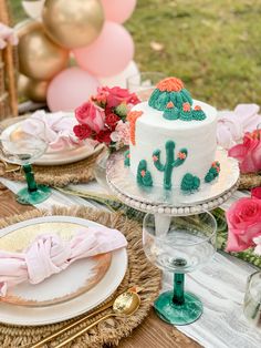 a table topped with a white cake covered in frosting and pink flowers next to balloons