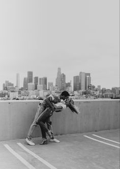 black and white photograph of two people kissing each other in front of a city skyline