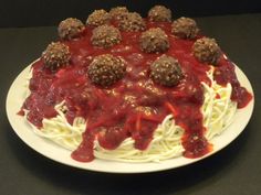 a cake covered in spaghetti and meatballs on top of a white plate with red sauce