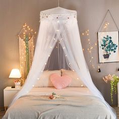 a white canopy bed in a bedroom with string lights on the ceiling and pink pillows