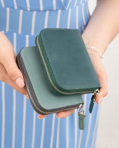 a woman is holding a green wallet with a keychain in her left hand