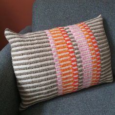 an orange and gray striped pillow on a blue chair with a brown arm rest in front of it