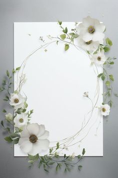 white flowers and greenery are arranged around the corner of a sheet of paper on a gray background