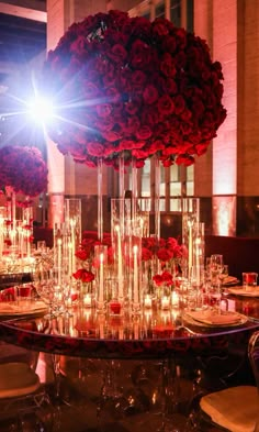 a table topped with lots of red roses and tall glass vases filled with candles