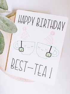 a happy birthday card with two tea cups on it next to a potted plant