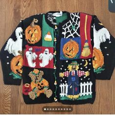 a black sweater with pumpkins, ghostes and other things on it sitting on a wooden floor