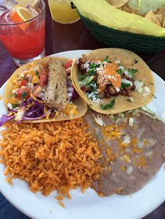 two tacos, rice and beans on a plate next to some drinks with orange wedges