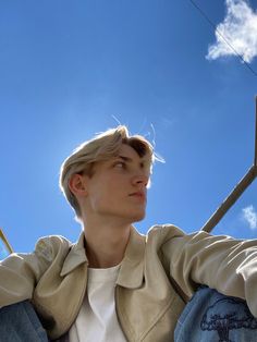 a woman sitting on top of a wooden bench under a blue sky with white clouds