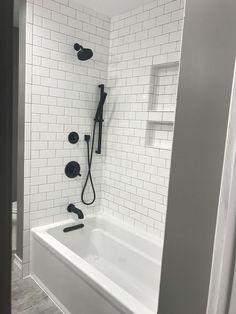 a white bathtub with black fixtures in the shower and tiled flooring on the walls