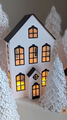 a paper house is lit up in front of some white trees and snow covered branches