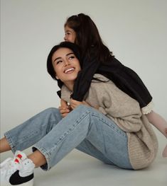 a woman sitting on the ground with her legs crossed and holding onto another woman's back