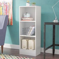 a white book shelf with baskets and books on it in front of a blue wall